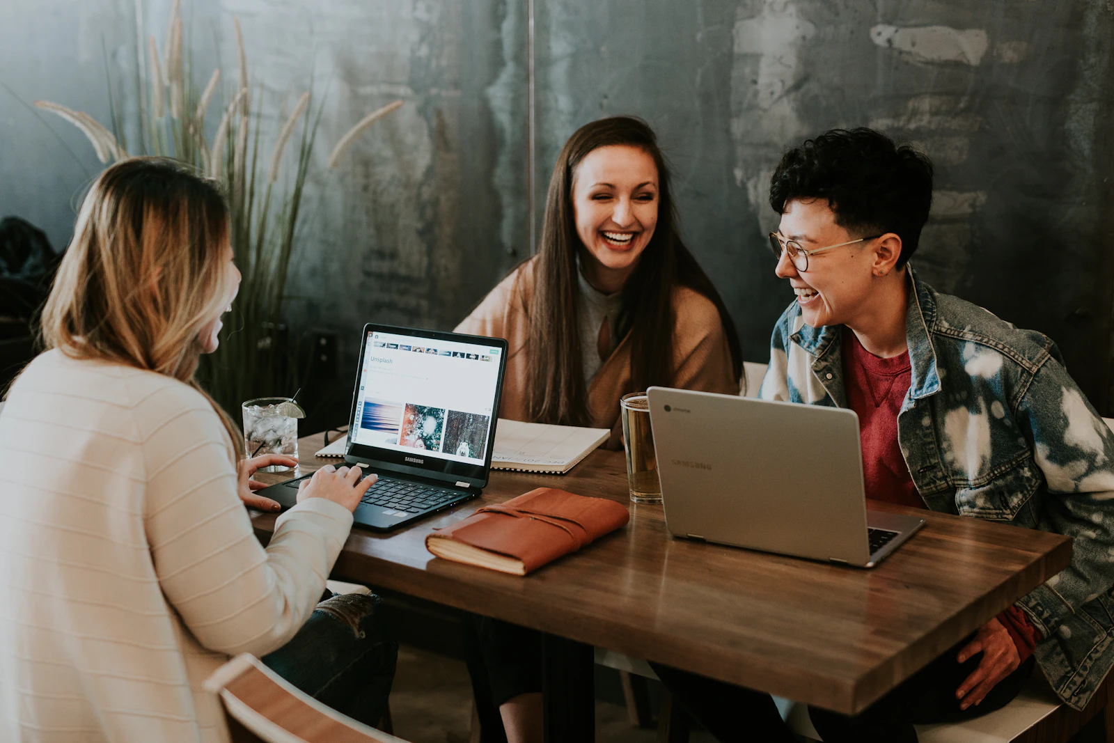 Three people laughing together at a table with laptops